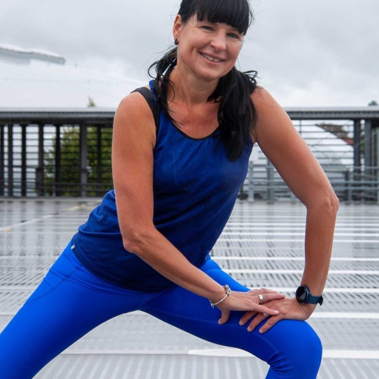 Eine Frau in blauer Sportbekleidung macht eine Dehnübung im Freien.