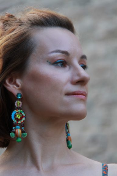 Schöne Frau mit dekorativem Ohrschmuck, vor einer Steinwand.
