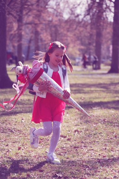 Ein Kind rennt im Park, eine Schultüte in der Hand. Schulanfang.
