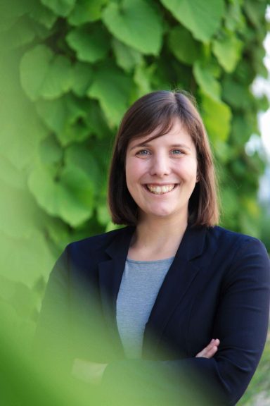 Junge Frau im Businessoutfit. Im Hintergrund grüne Blätter.
