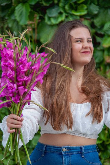 Junge Frau mit langen, braunen Haaren hält einen Strauß lila Gladiolen in der Hand.