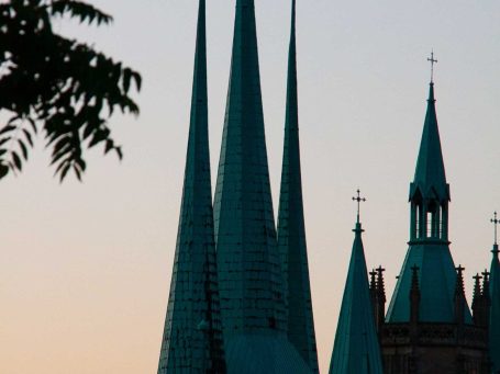 Silhouette von Kirchtürmen mit spitzen, grünlich-blauen Dächern bei Sonnenuntergang.