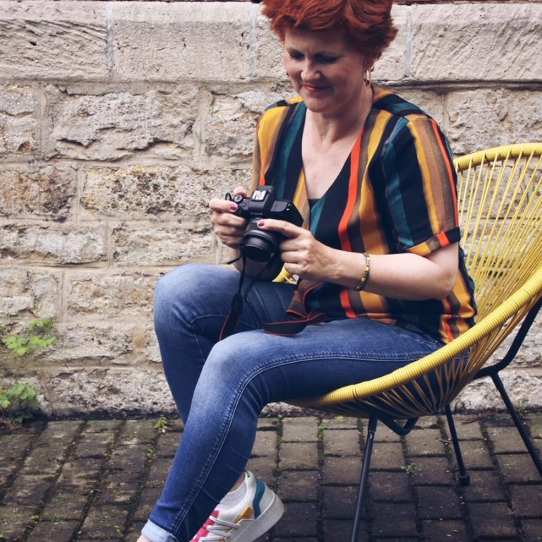Frau mit Kamera in der Hand in farbiger Umgebung vor einer Steinwand.